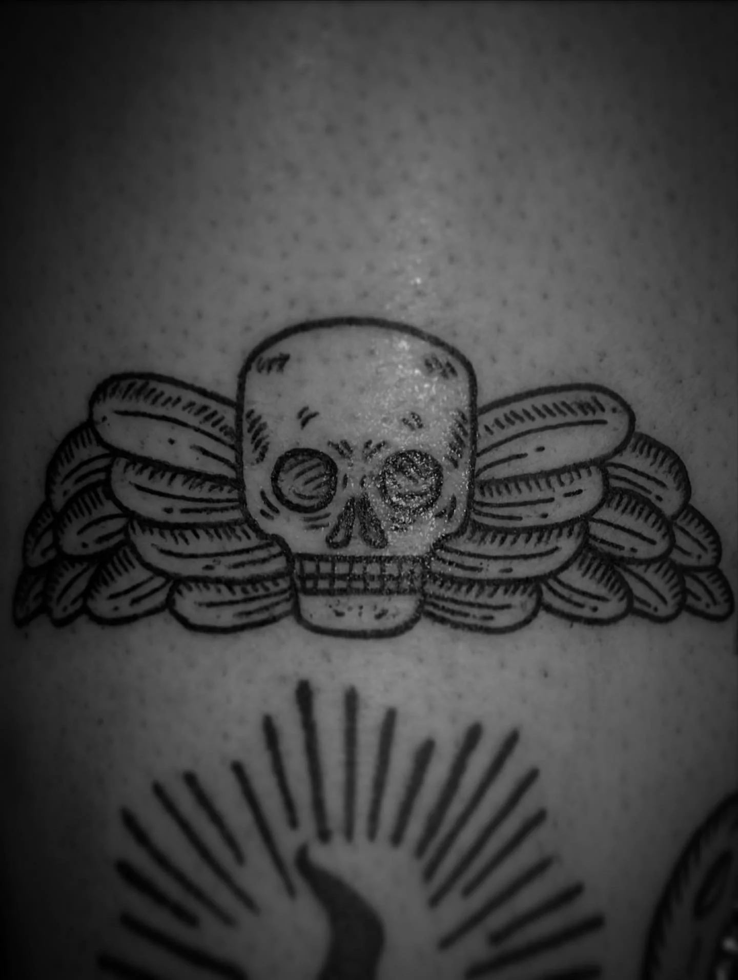 Black ink skull tattoo with wings.