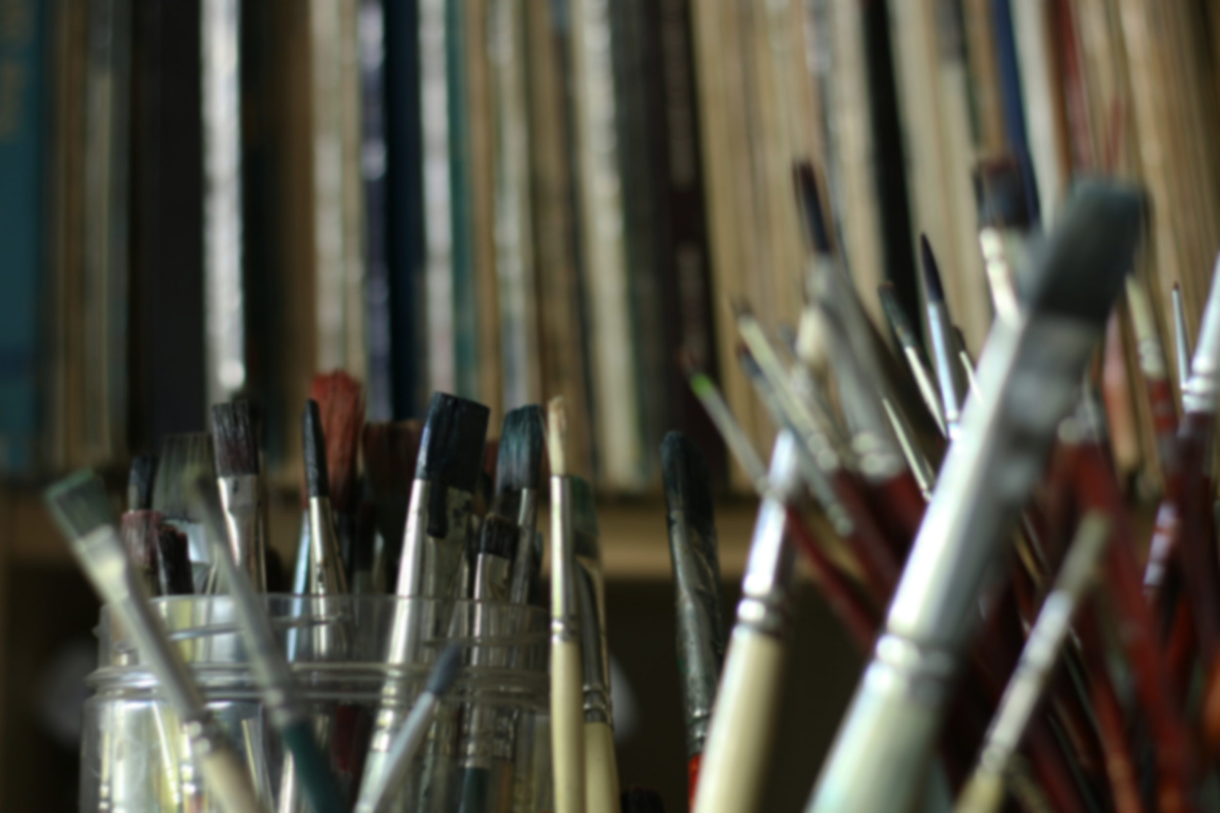 Close-up of paintbrushes arranged in a holder, with shelves of books blurred in the background.