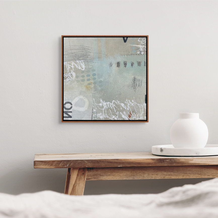 Abstract art painting hanging on a white wall above a wooden table with a white vase and tray.