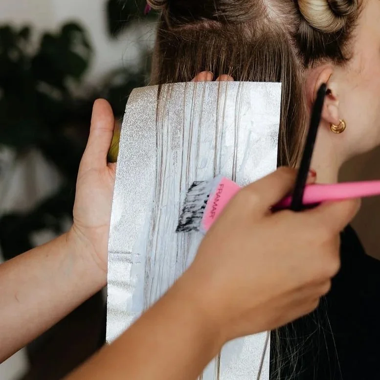 A person getting a haircut, with foil covering part of their hair, while a stylist uses scissors and a comb to cut the hair.