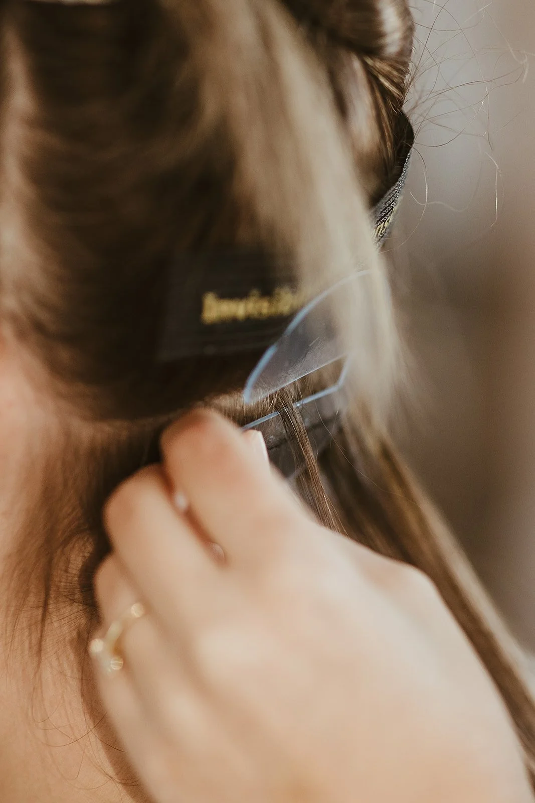 Close-up of a person adjusting a transparent face shield near their ear, wearing a gold ring on their finger.
