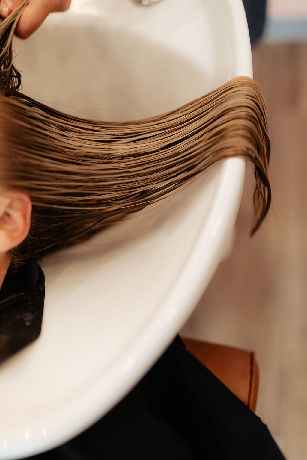 Hairdresser rinsing hair in a white salon sink.