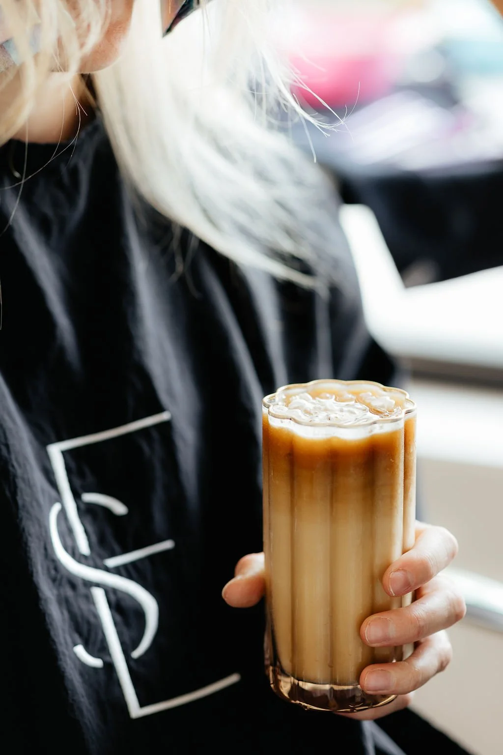 Person holding a tall glass of iced coffee with milk and ice cubes inside.