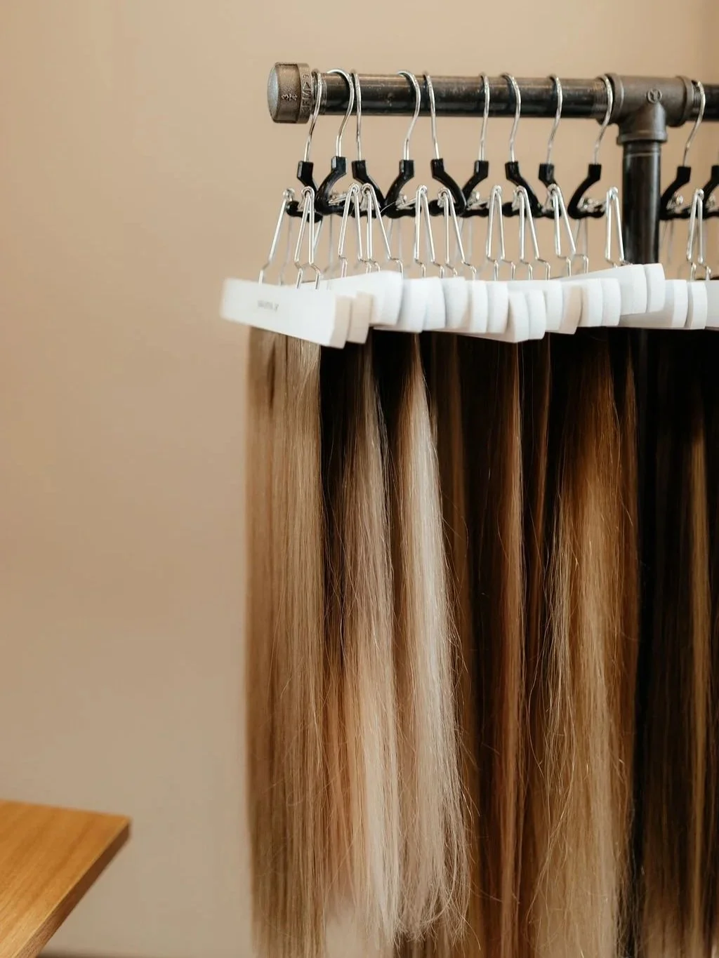 Hair extensions hanging on a metal rack with beige wall background.
