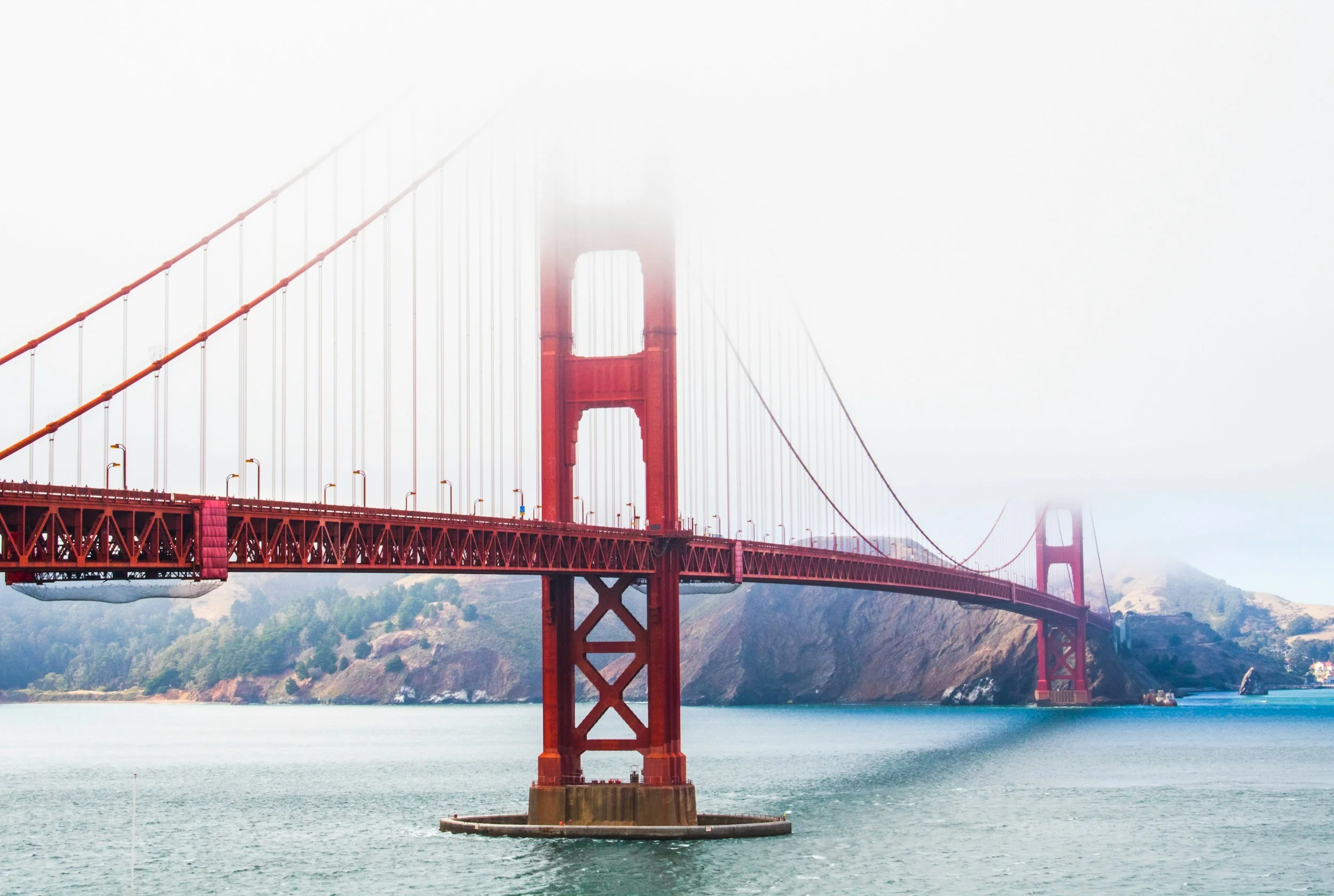 The Golden Gate Bridge in San Francisco, California, shrouded in fog with water and hills in the background.