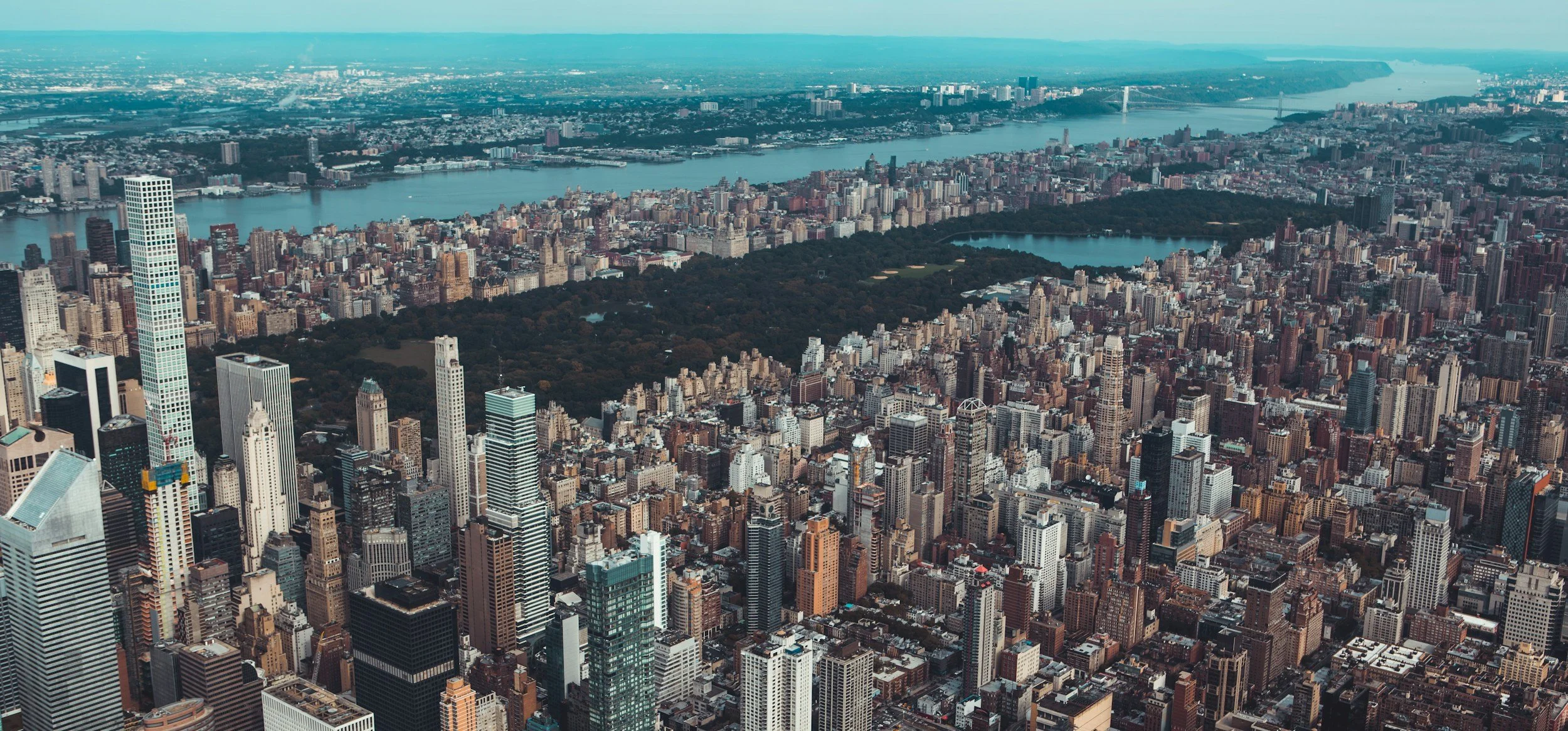 Aerial view of New York City skyline with tall skyscrapers, Central Park, and the Hudson River.