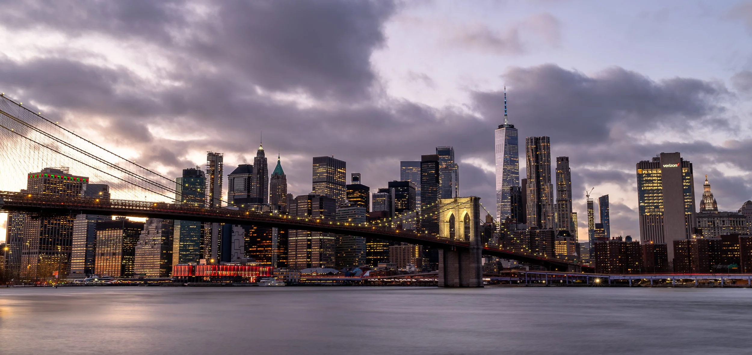 Night view of Toronto city skyline with the CN Tower illuminated, boats docked at marinas along the waterfront, and city lights reflected on the water.