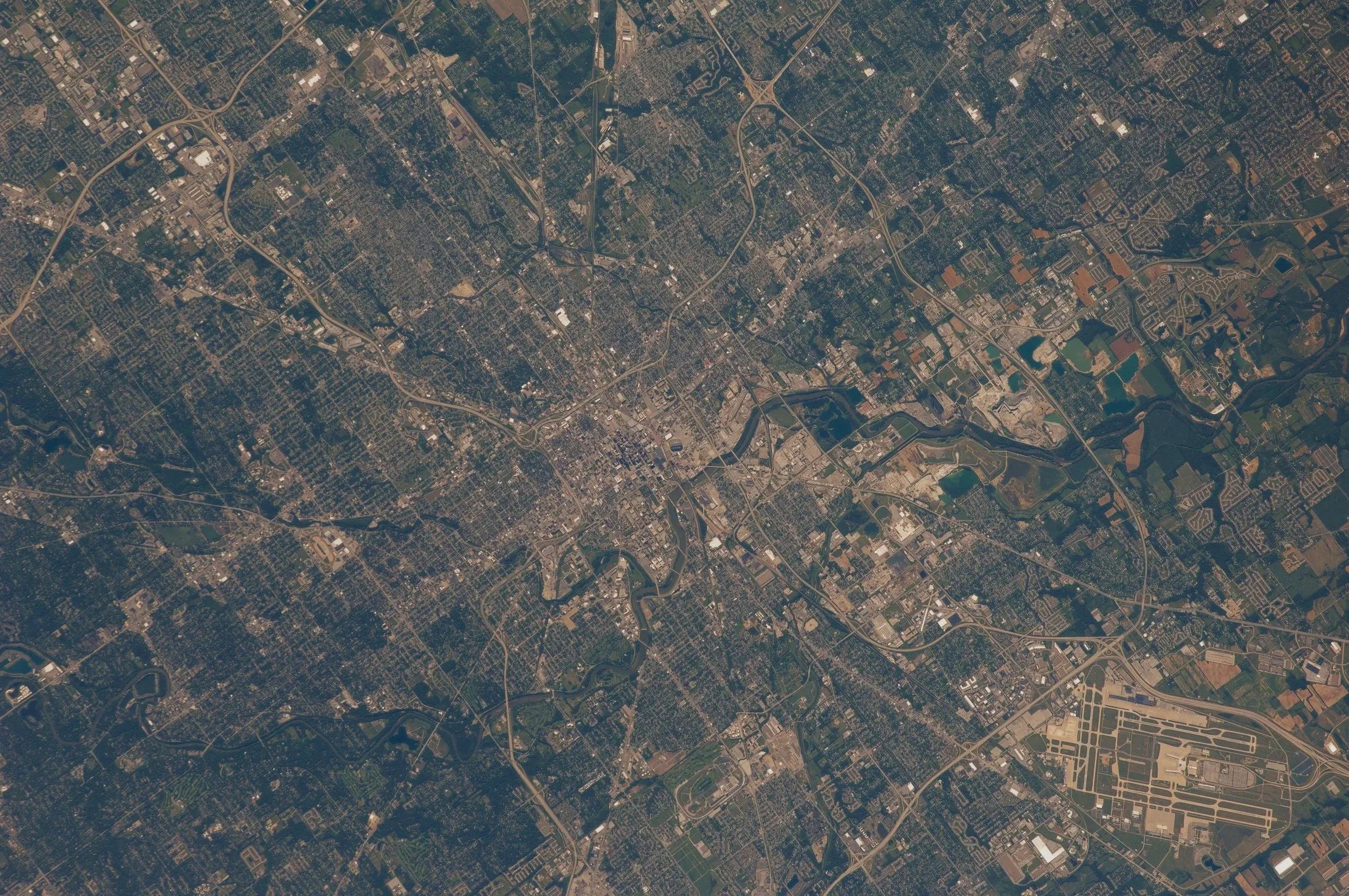 An aerial view of a city with roads, rivers, and buildings, including an airport with runways and surrounding infrastructure.