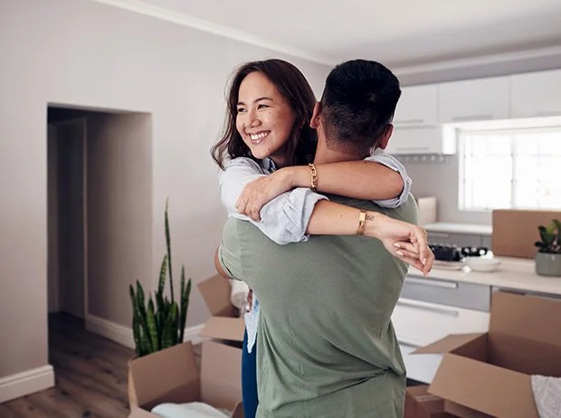 A woman smiling as she is hugged by a man in a modern kitchen with open boxes around.