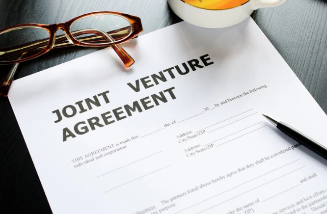 A joint venture agreement document on a desk with a pair of eyeglasses, a pen, and a cup of coffee nearby.