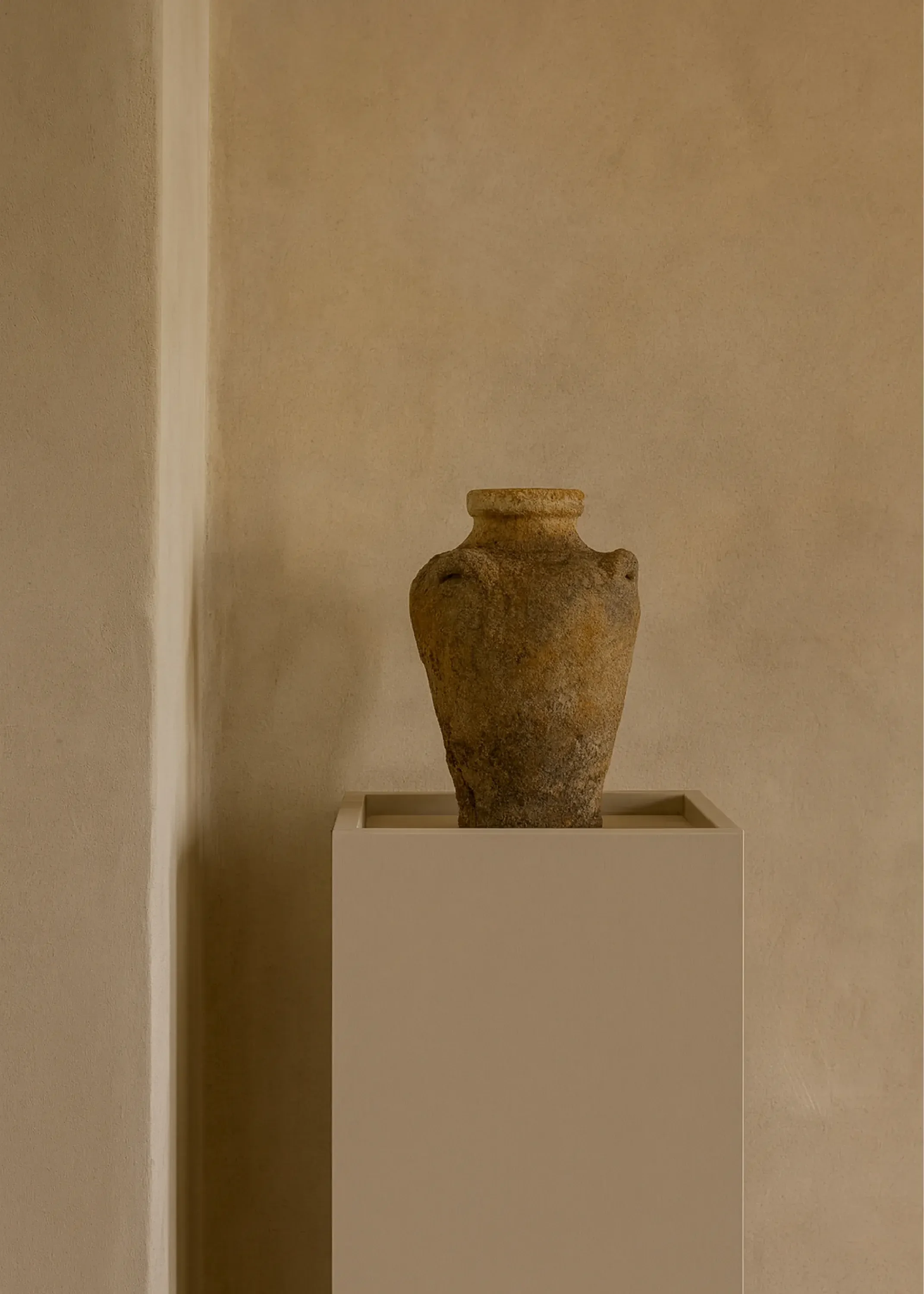 Ancient ceramic vase displayed on a white pedestal in a museum setting.