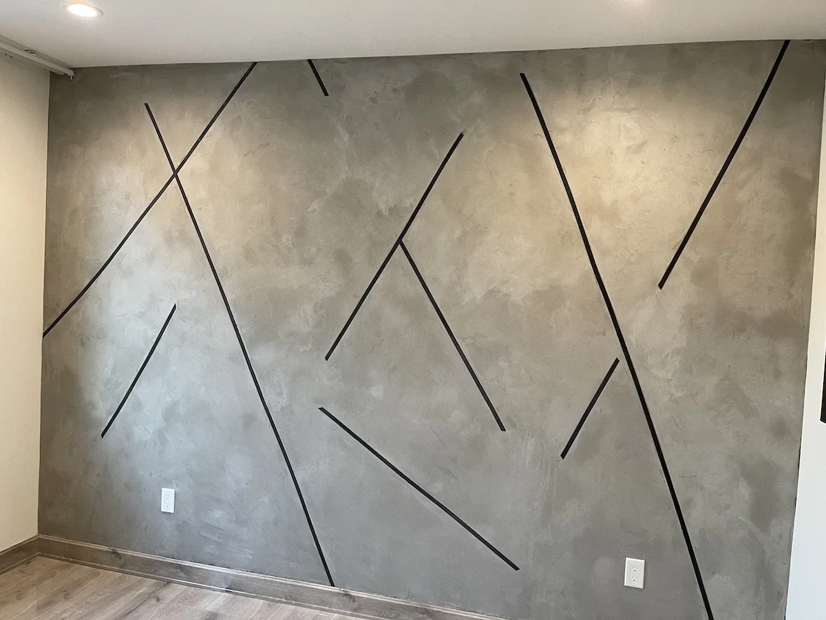A large modern accent wall with a smooth grey concrete plaster finish and a custom black geometric line design.