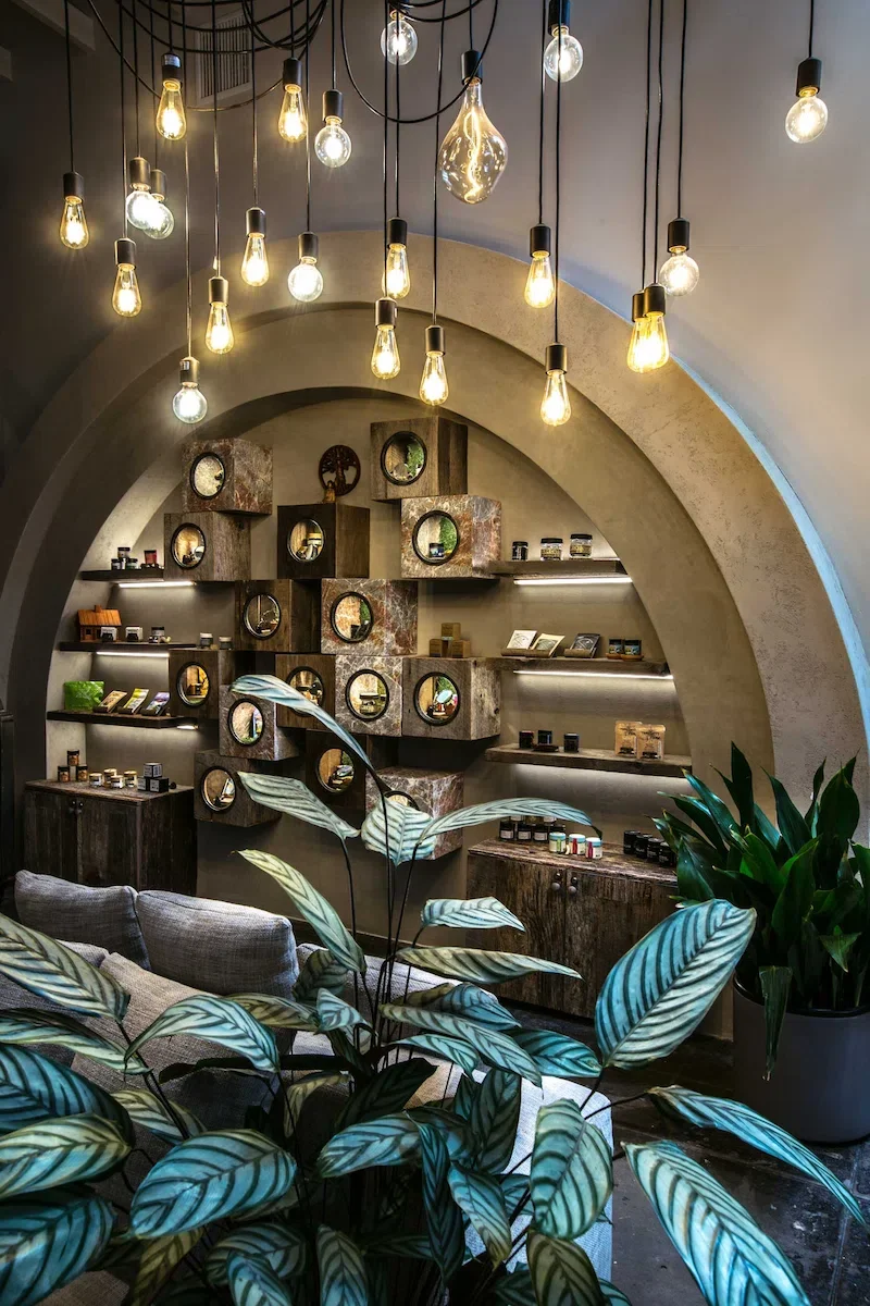 Atmospheric wide shot of a large Venetian plaster arch with a custom geometric wood display and hanging Edison bulb lighting at The Woods West Hollywood.