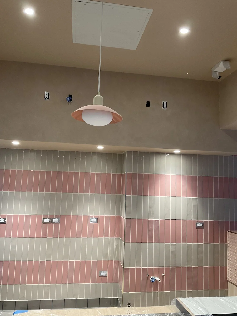 Minimalist warm-toned Venetian plaster finish on a restaurant bulkhead above pink and grey tiled walls at Sweetfin Beverly Hills.