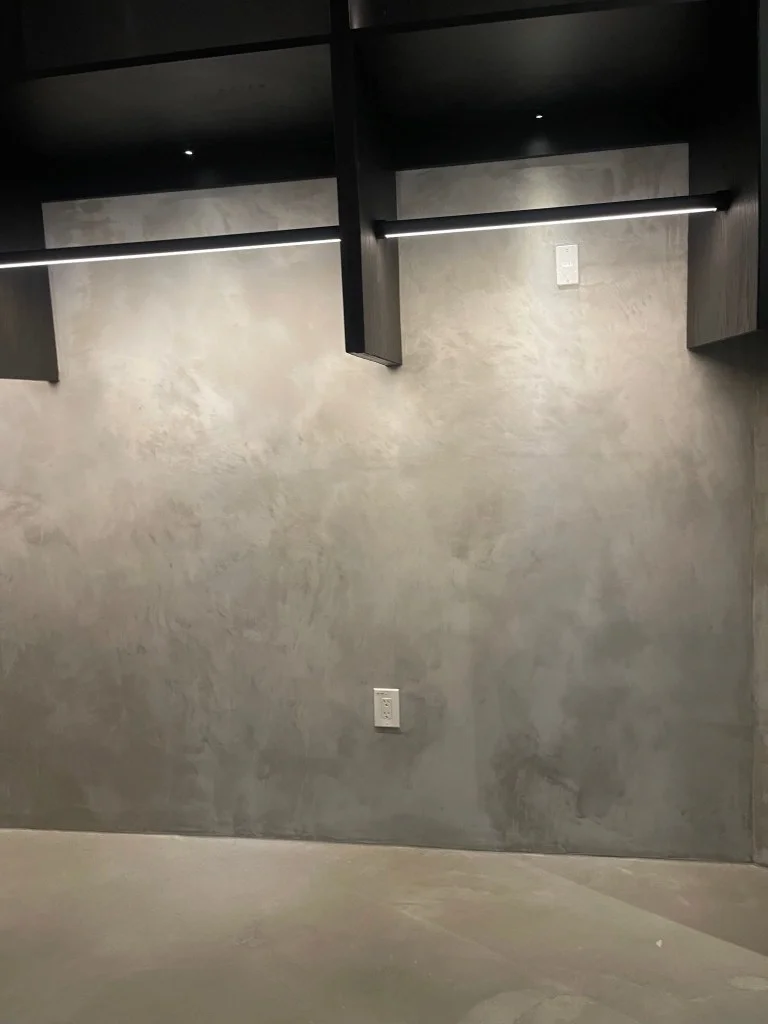 A high-end minimalist closet back wall with a grey concrete-finish plaster and dark custom wood shelving.