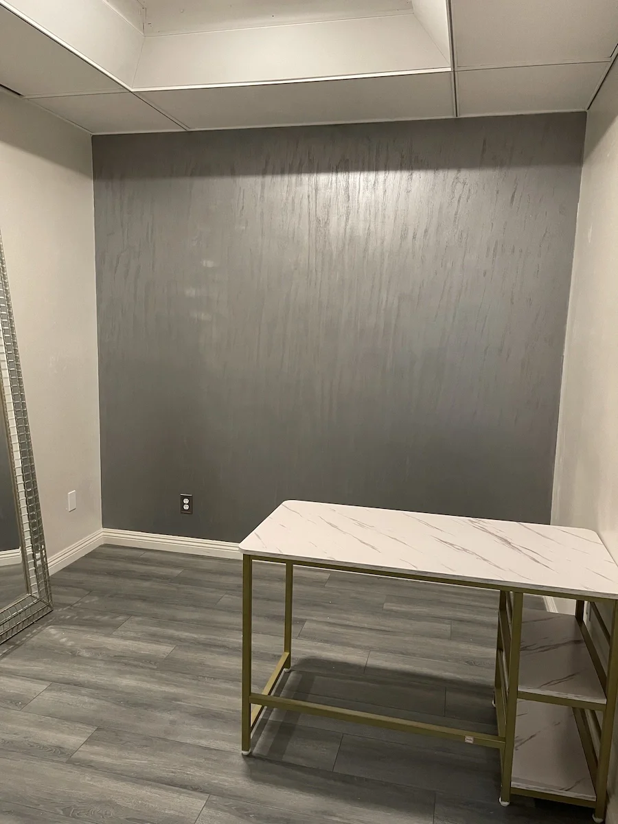 Finished charcoal grey metallic Venetian plaster accent wall in a salon treatment room with a modern marble desk.
