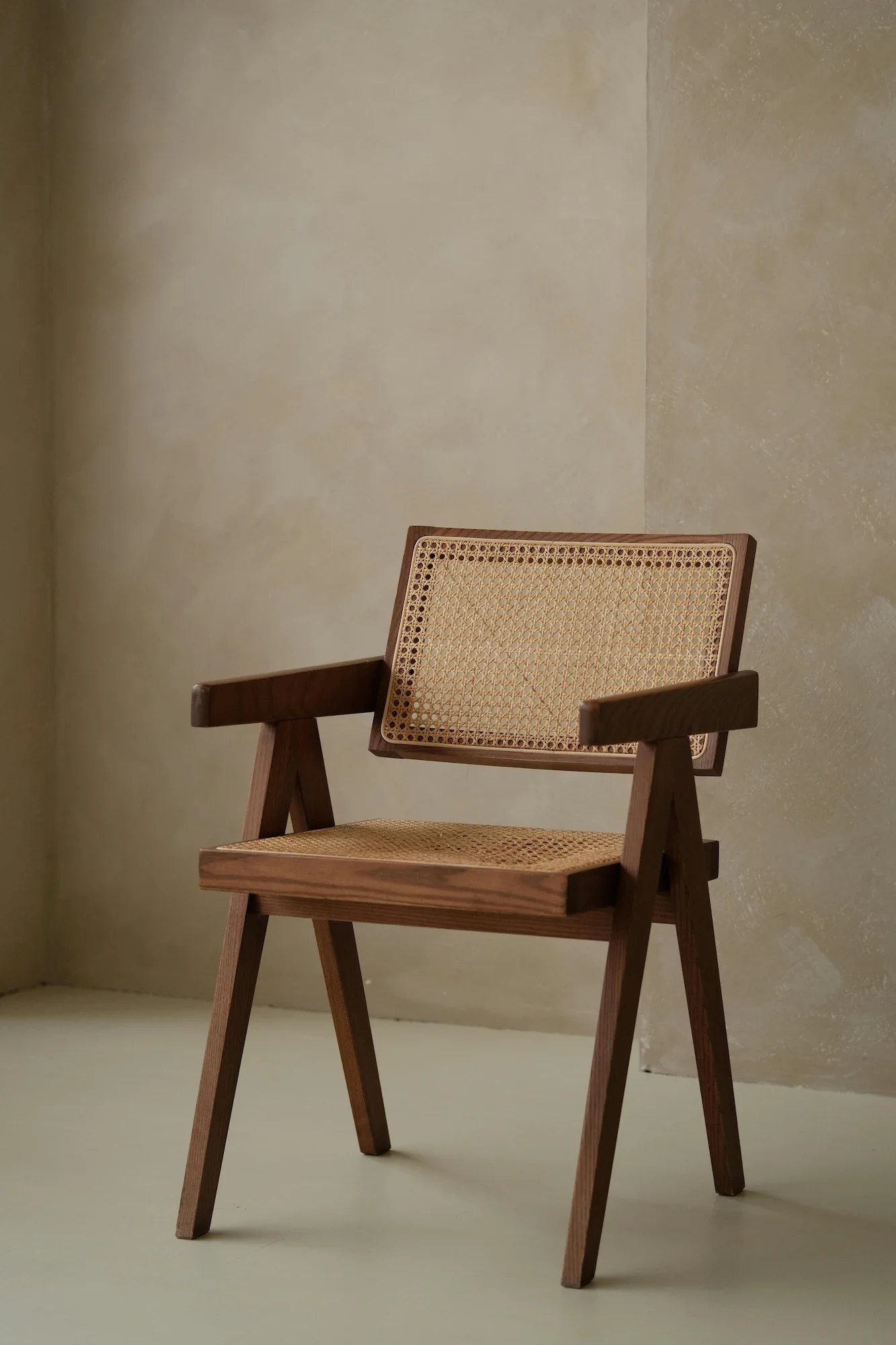 Minimalist corner featuring a textured beige plaster wall with organic trowel marks, serving as a serene, wabi-sabi backdrop for a mid-century modern wooden cane chair.