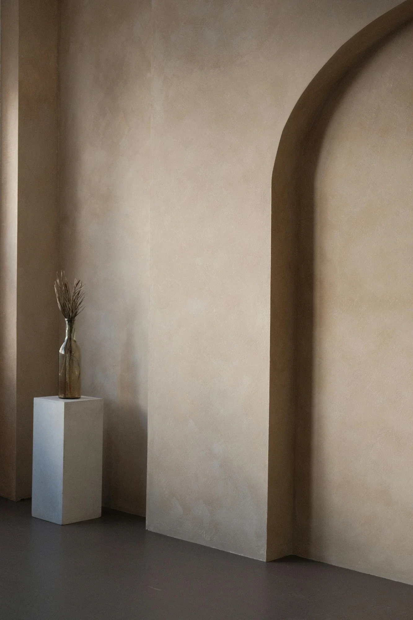 A minimalist interior featuring a large architectural arch finished in a warm sand-toned Suede Finish Venetian plaster, showcasing hand-applied texture and soft, organic movement.