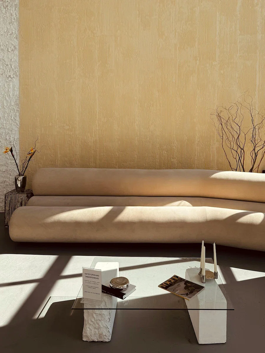 Minimalist living room with vertical linear textured plaster wall, curved beige sofa, and glass coffee table.