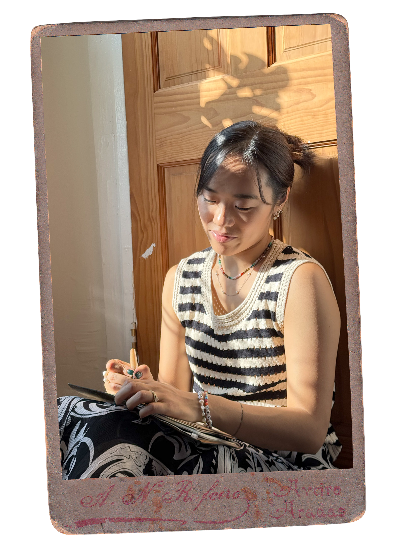 Carolyn by a wooden door, drawing or writing in a notebook in warm sunlight