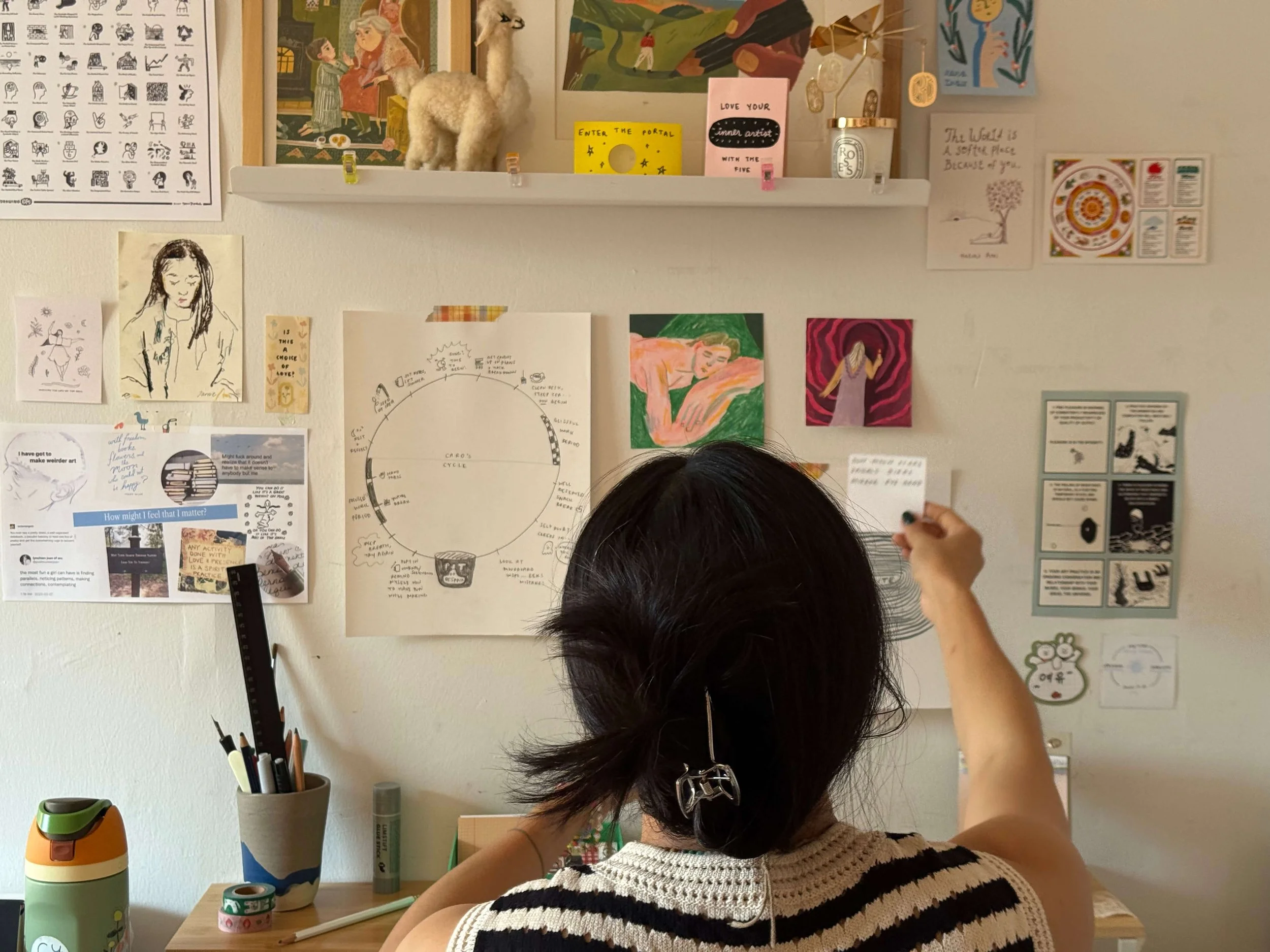 Carolyn Yoo working at her desk, adding notes to a wall of sketches and journal pages.