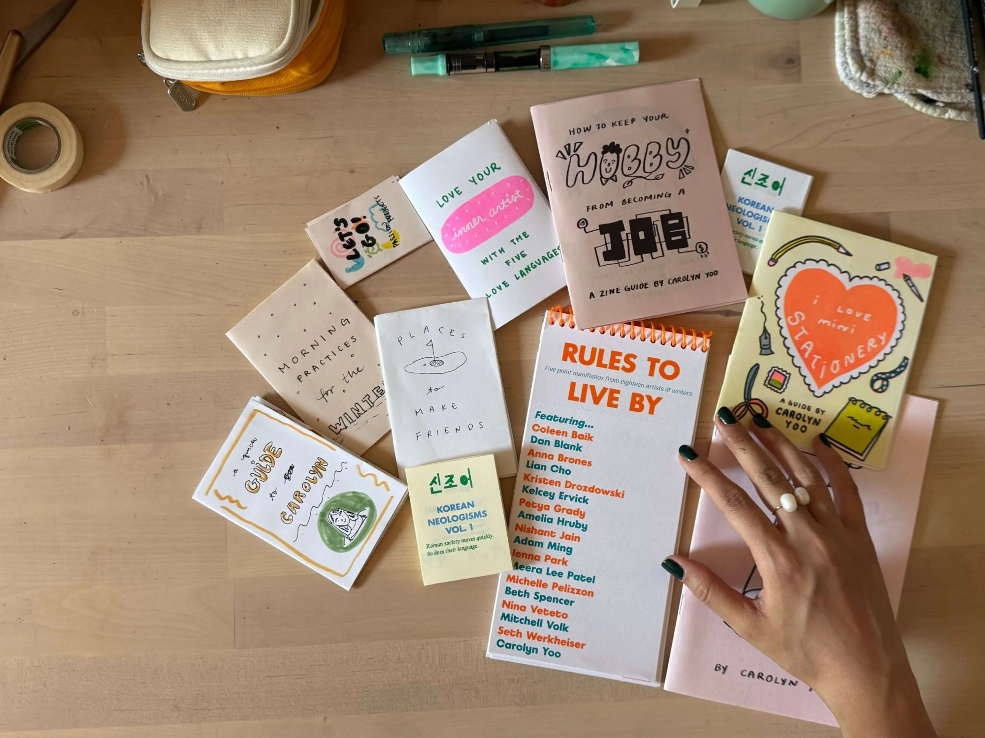 Carolyn Yoo’s hand arranging a collection of her handmade zines on a desk.