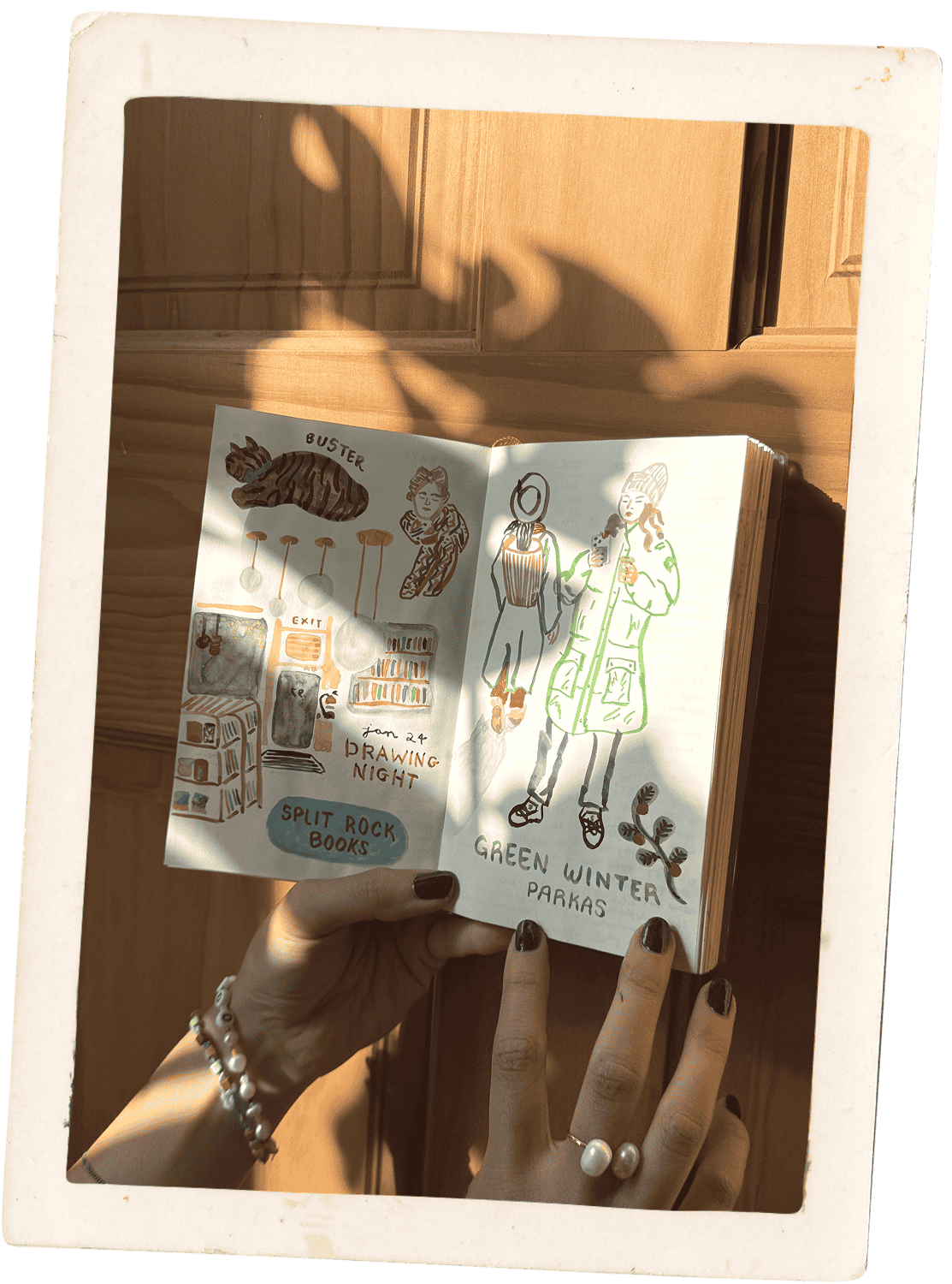 Carolyn Yoo holding an illustrated sketchbook open to drawings of books and winter outfits.