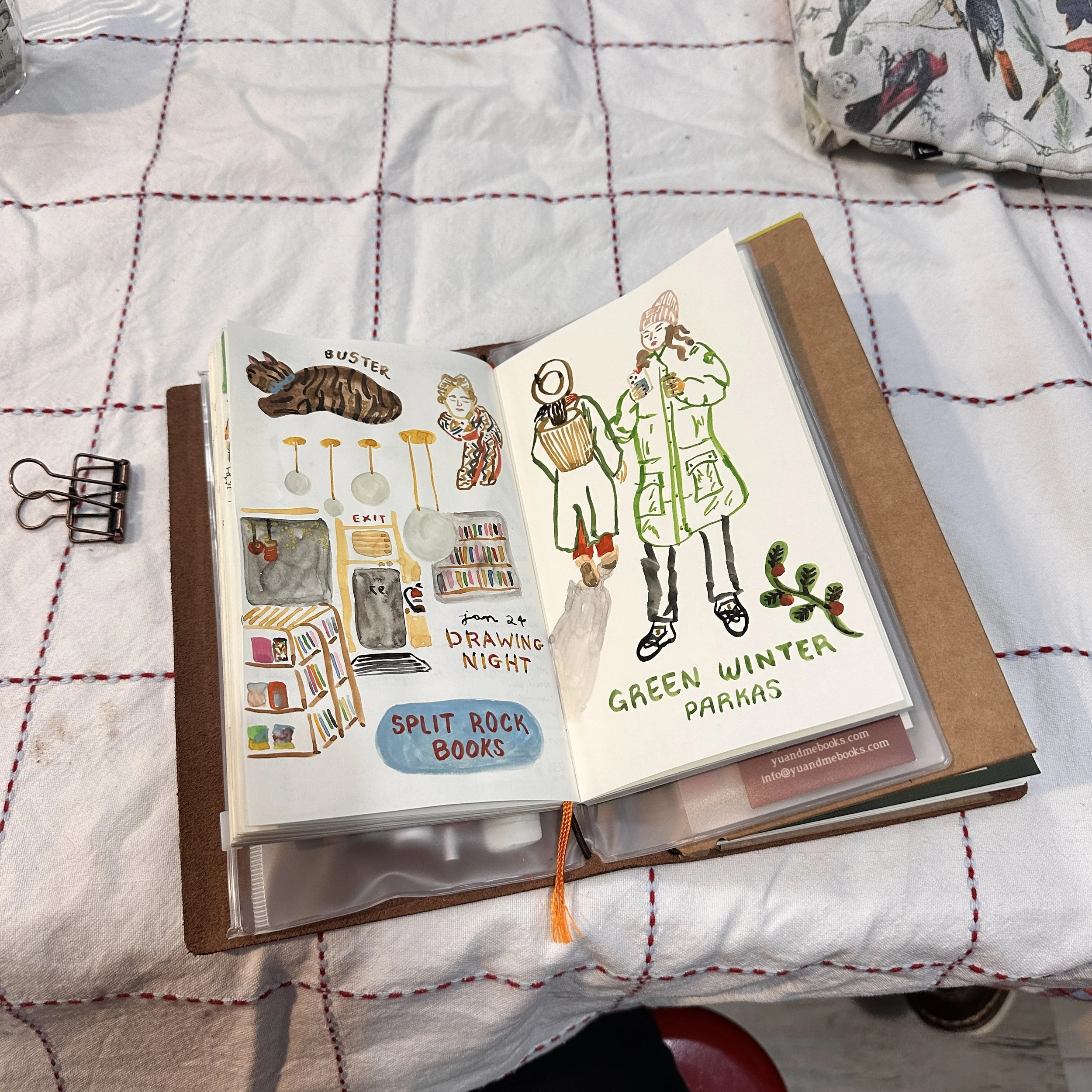 Open sketchbook on a table with illustrations of book shopping and winter fashion, surrounded by a white tablecloth with red checkered pattern.