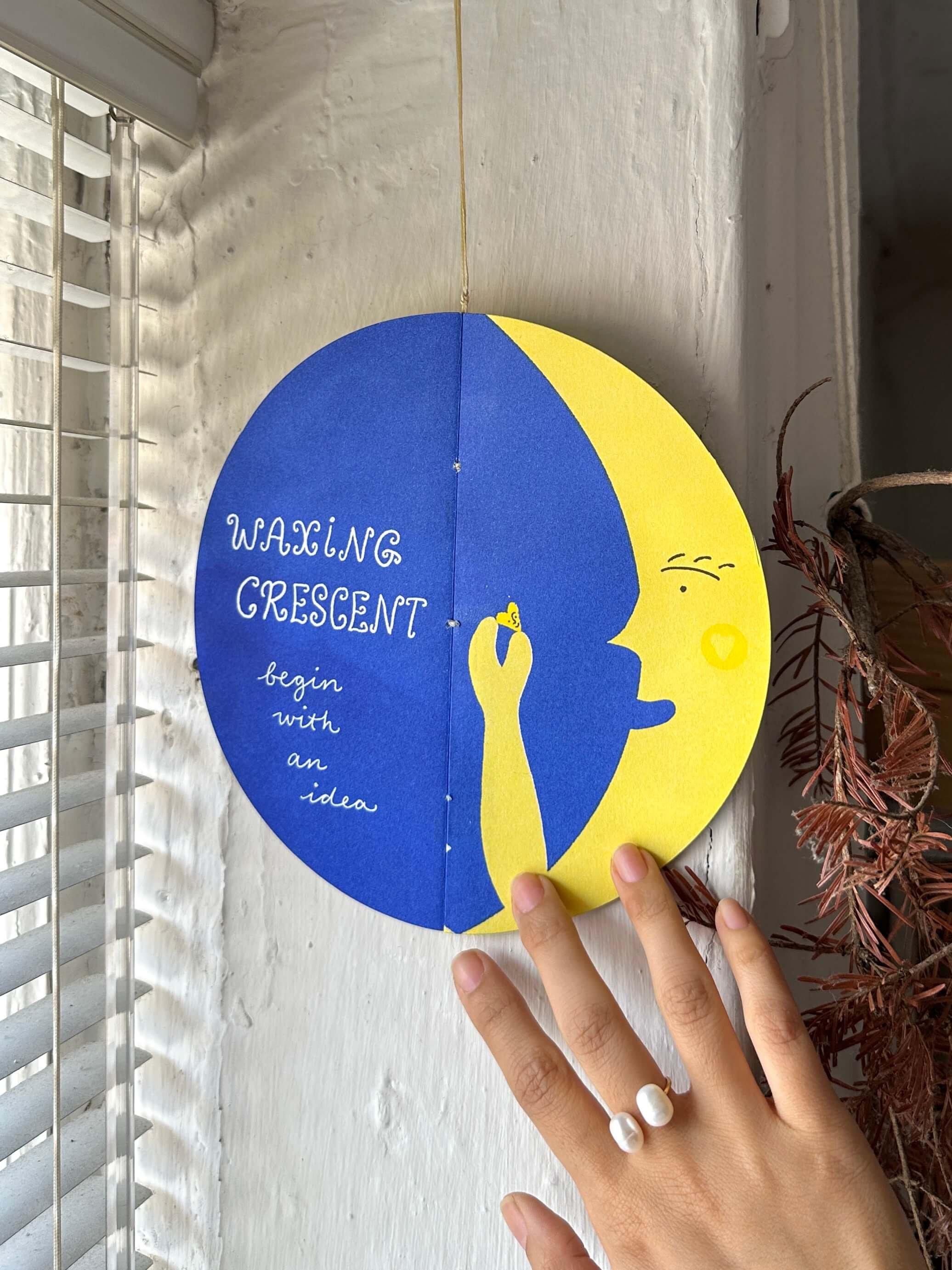 Hand holding a circular zine titled “Waxing Crescent — begin with an idea.”