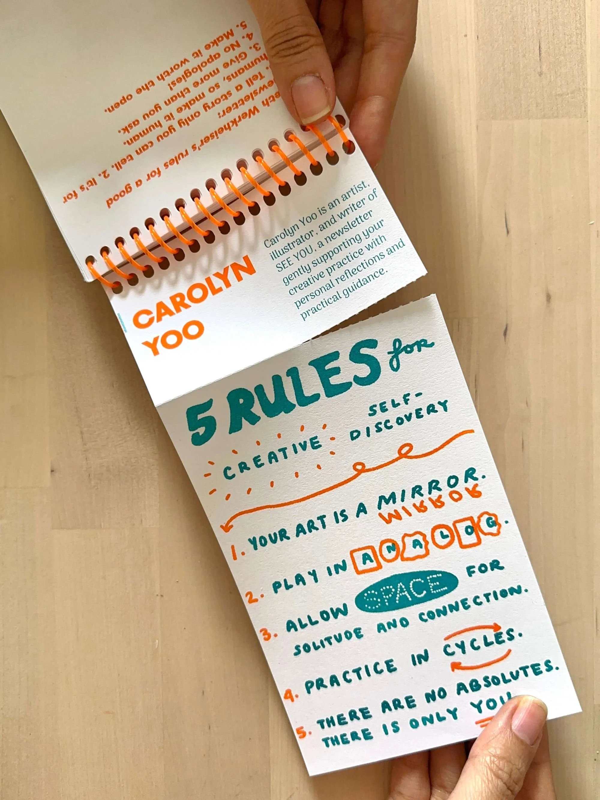 Hand holding a spiral-bound zine titled “5 Rules to Live By,” illustrated by Carolyn Yoo.