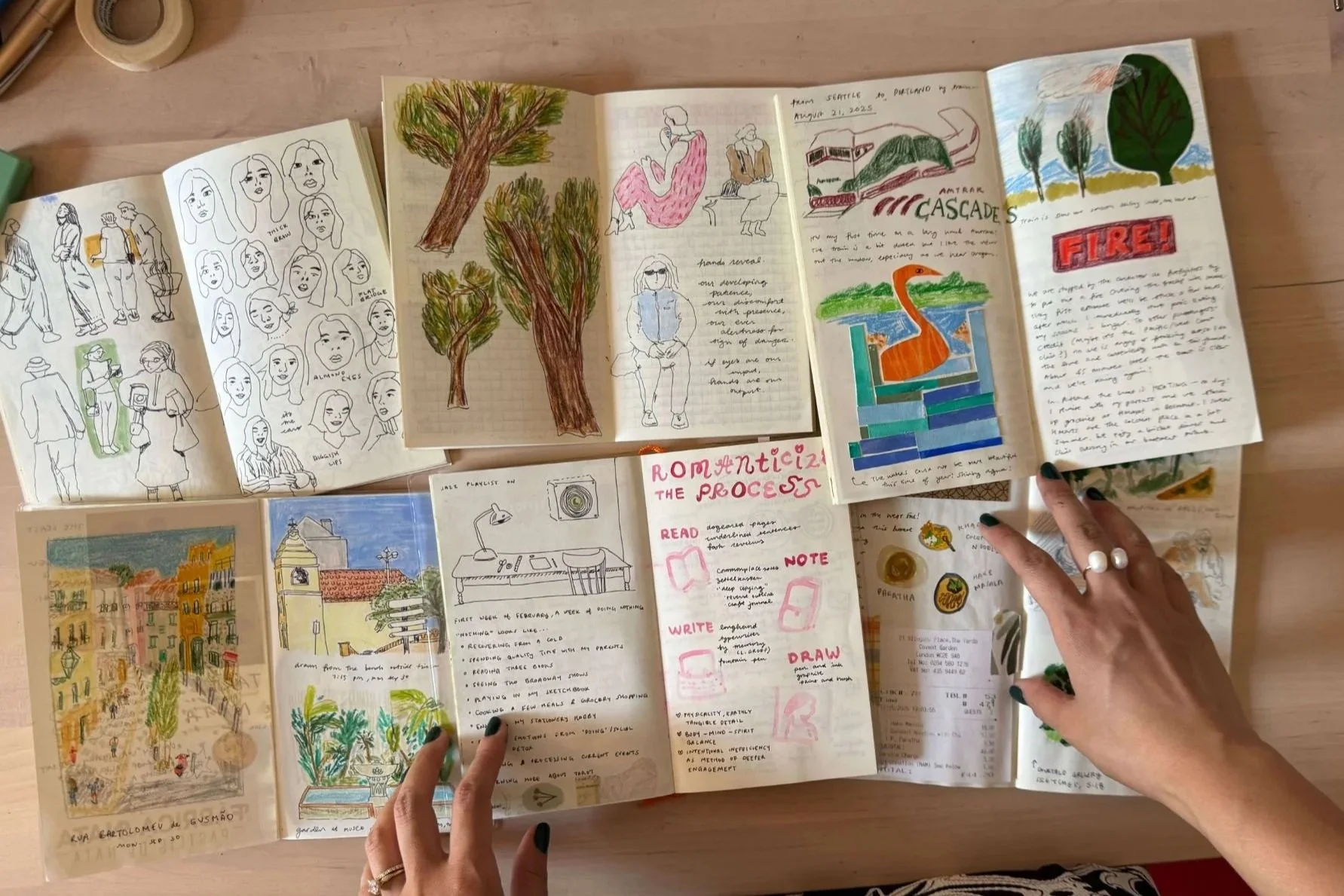 Open notebooks and sketches on a wooden table, showing drawings of trees, people, cityscape, a swan-shaped river, and handwritten notes.