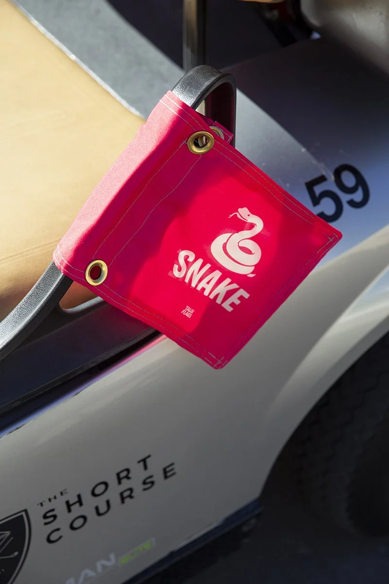 A red fabric bag with a snake logo and the word "SNAKE" on it, attached to the side of a vehicle with the logo "The Short Course."