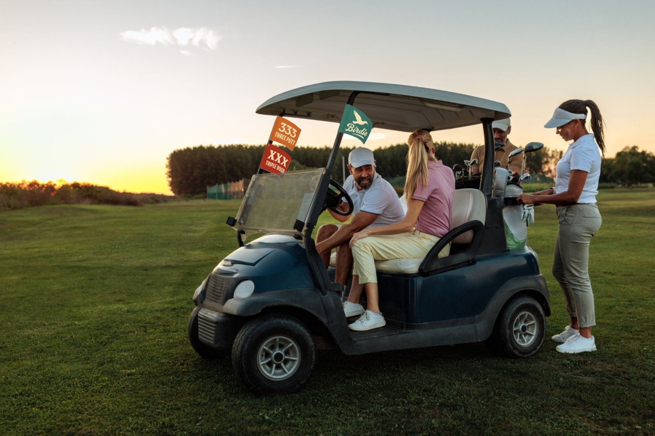 Four people on a golf course around a golf cart at sunset, two sitting inside the cart and two standing outside, with golf clubs and bags.