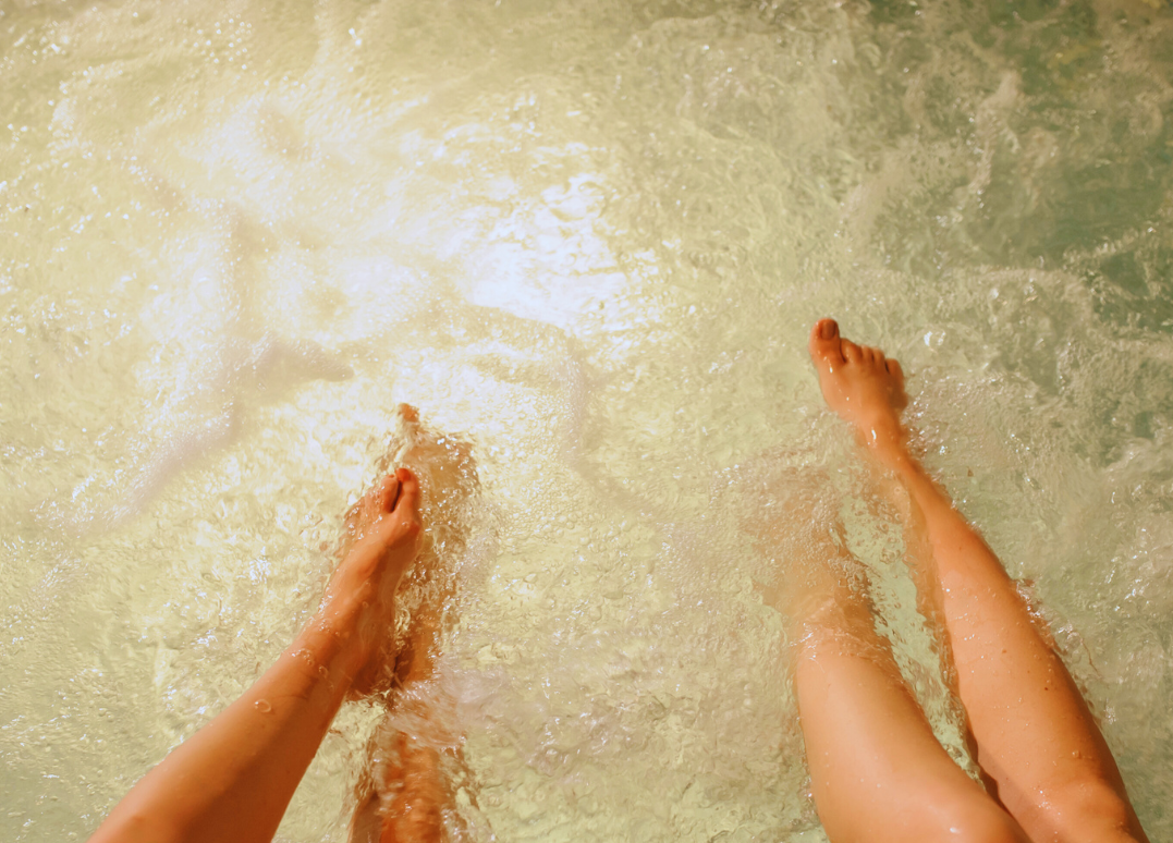 Two people soaking their legs in a warm bath or pool with bubbling water.