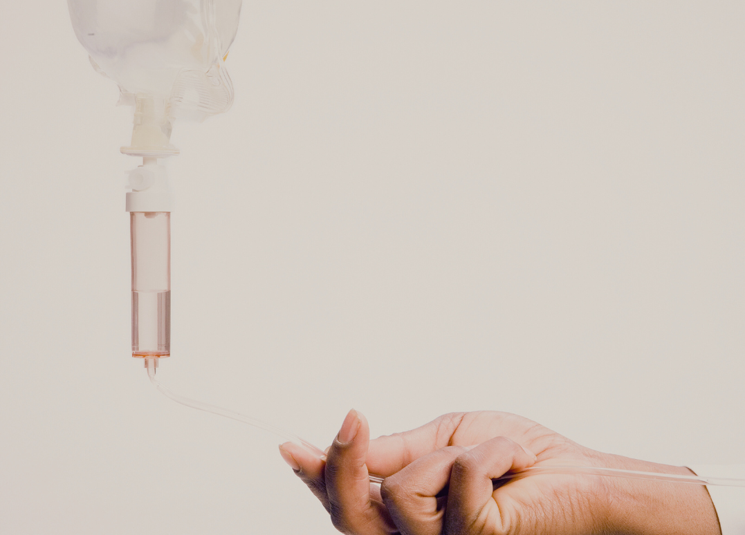 Close-up of a hand holding a medical IV tube, with an IV bag hanging above.