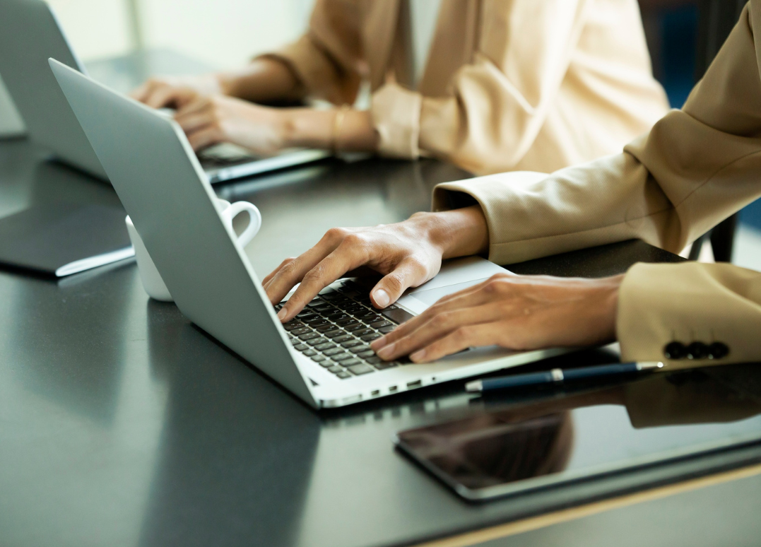 People working on laptops at a table with notebooks, pens, and a tablet.