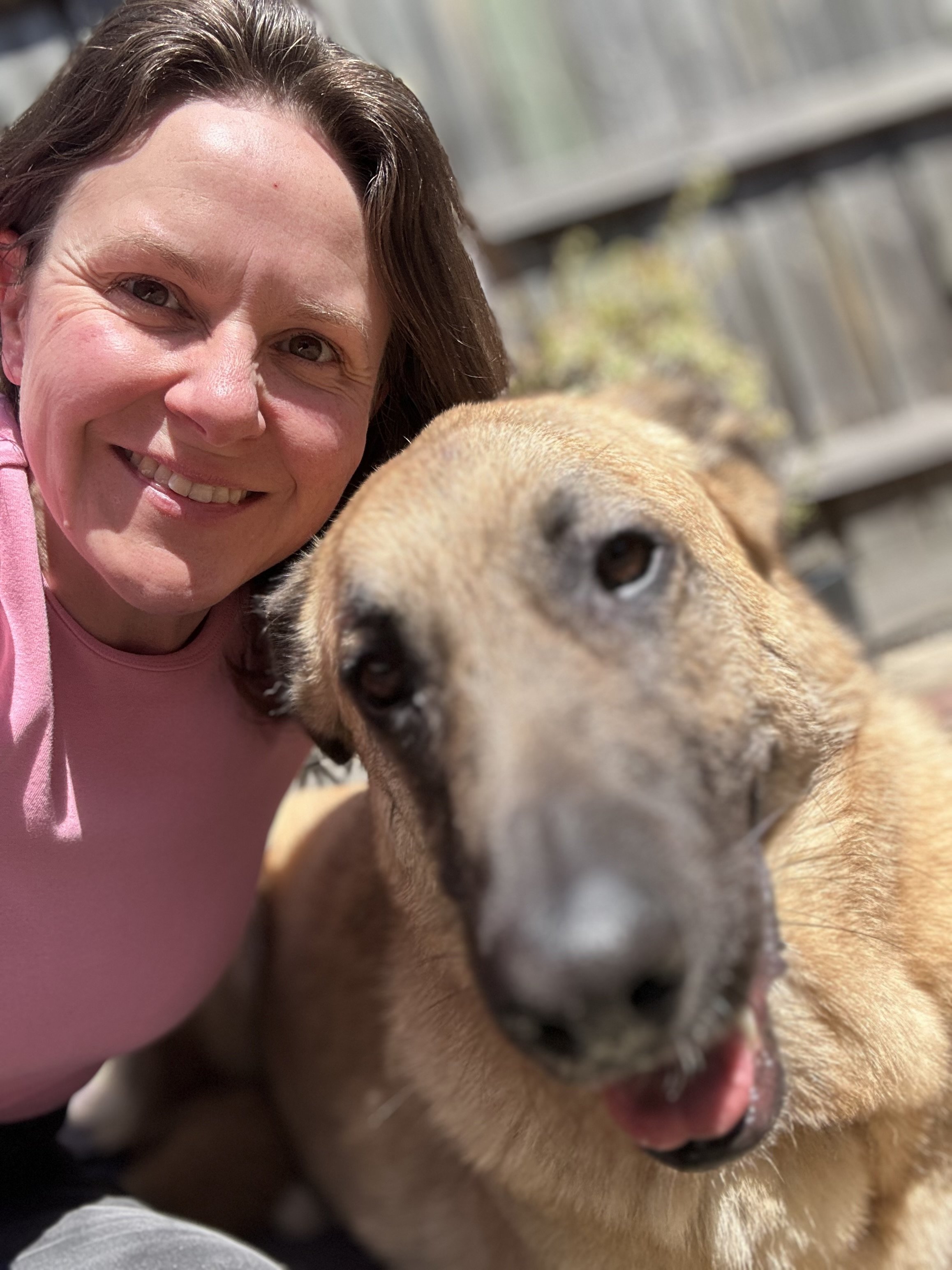 A woman smiling with a tan-colored dog.