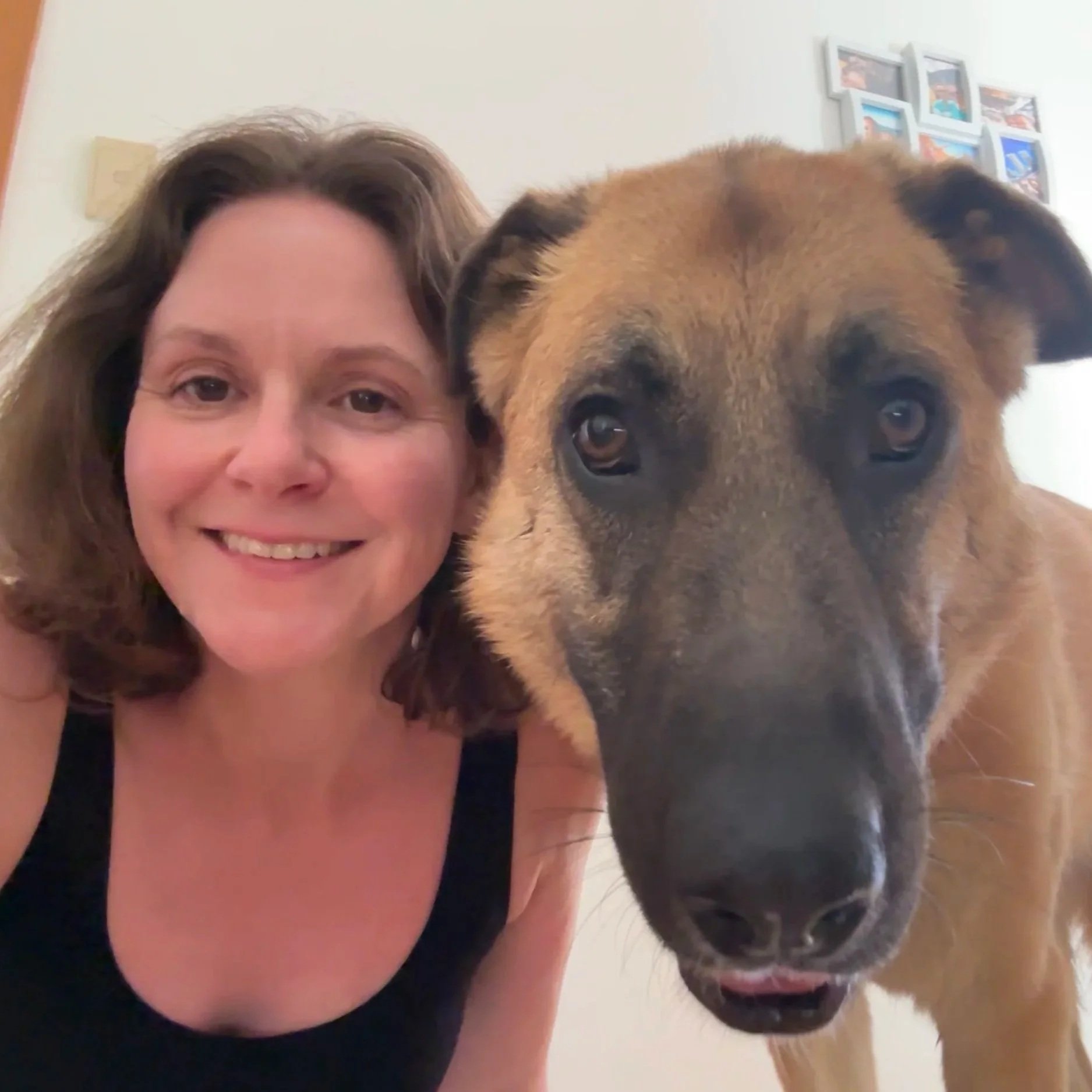 A smiling woman in a black tank top taking a selfie with a large brown dog with black markings.