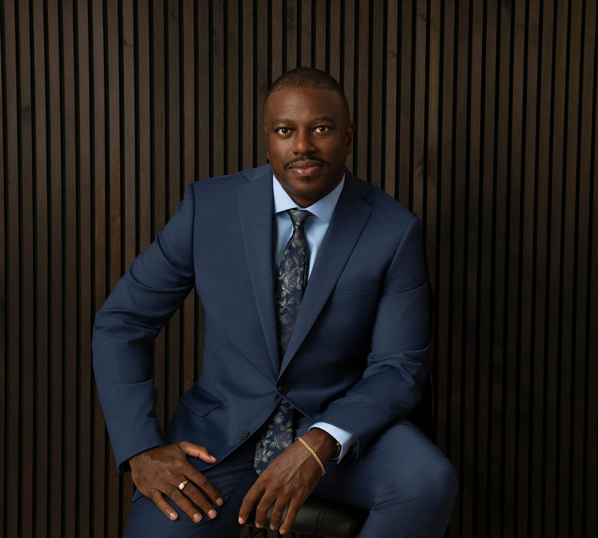 Professional photo of Dr. Winston Irving, founder of Irving Radiology. He is sitting in front of a wooden slatted background wearing a navy blue suit