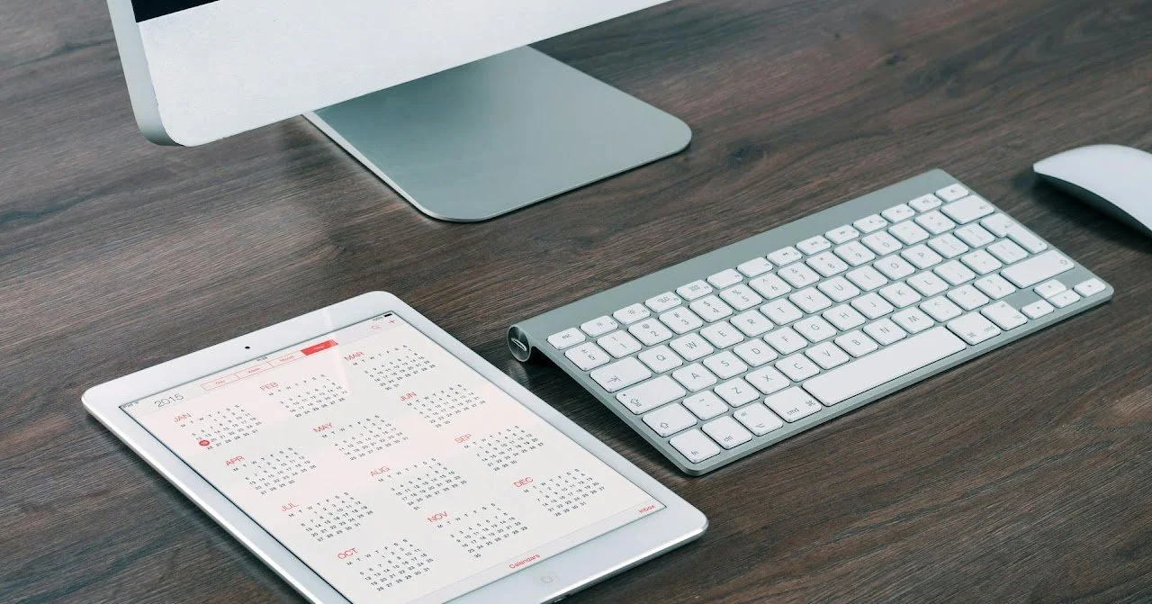 Desk with a computer monitor, a wireless keyboard, a wireless mouse, and a tablet displaying a 2016 calendar.