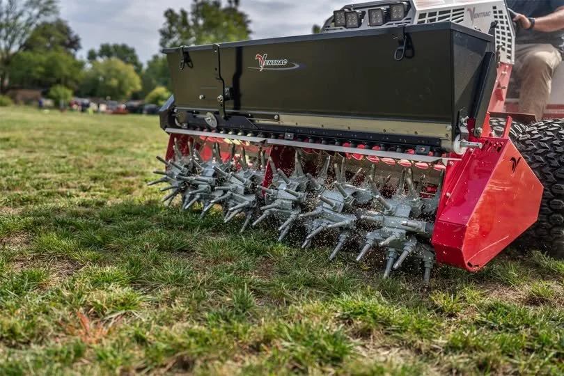 Close-up of a large, red and black aerator machine with rotating blades working on a grassy field outdoors.