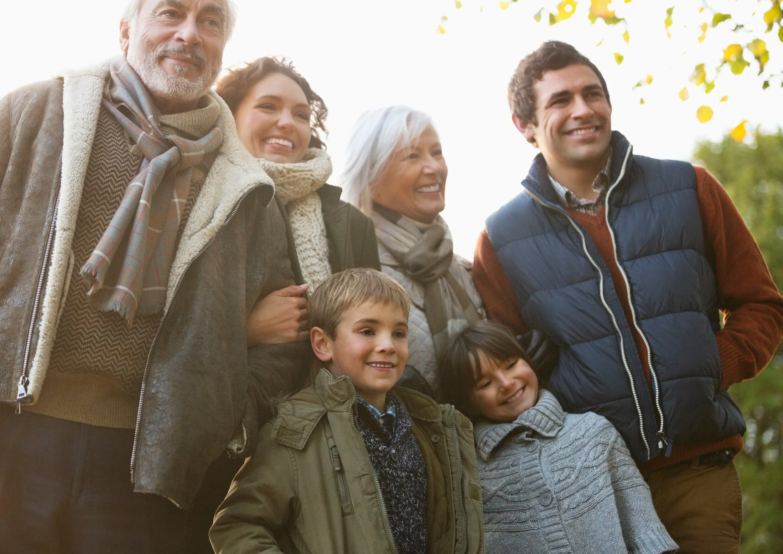 Multi-generational family traveling in cold-weather clothes and smiling for someone taking their photo (off camera)