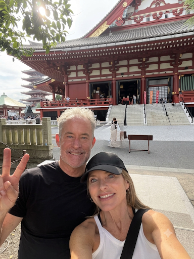 A smiling couple taking a selfie in front of a red temple and pagoda in Japan.