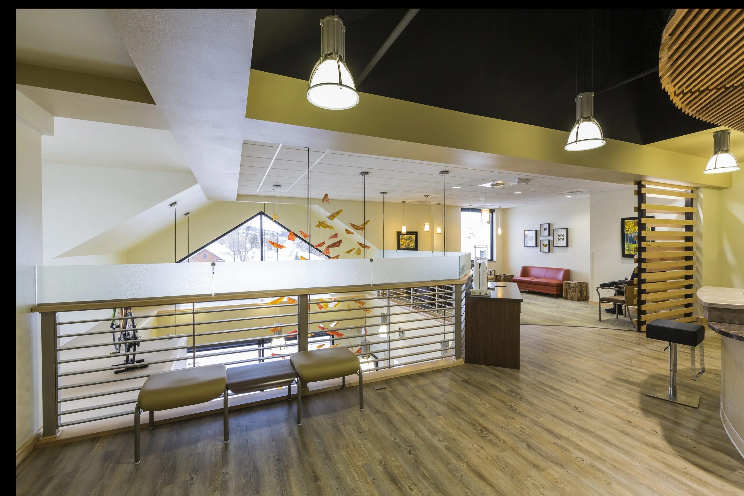 Interior of a modern building with a sitting area, large windows, hanging lights, and decorative artwork featuring flying insects or butterflies.