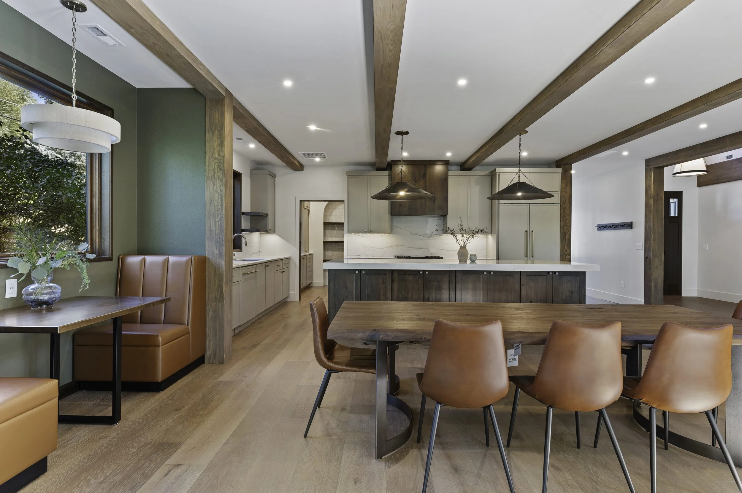 Modern open kitchen and dining area with wooden beams, central island, beige and gray cabinets, and pendant lighting.