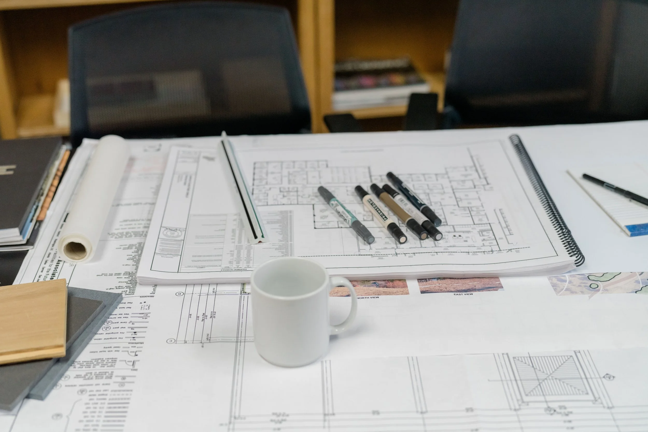 Architectural blueprints and drawing tools on a table, with a white coffee mug in the center.