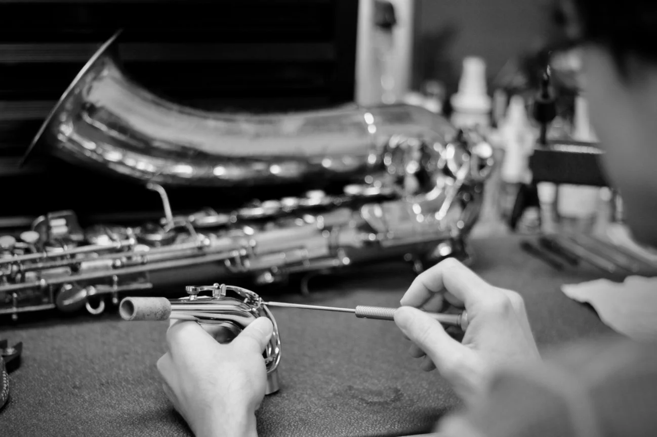Hand cleaning a saxophone with a cleaning rod in a workshop.