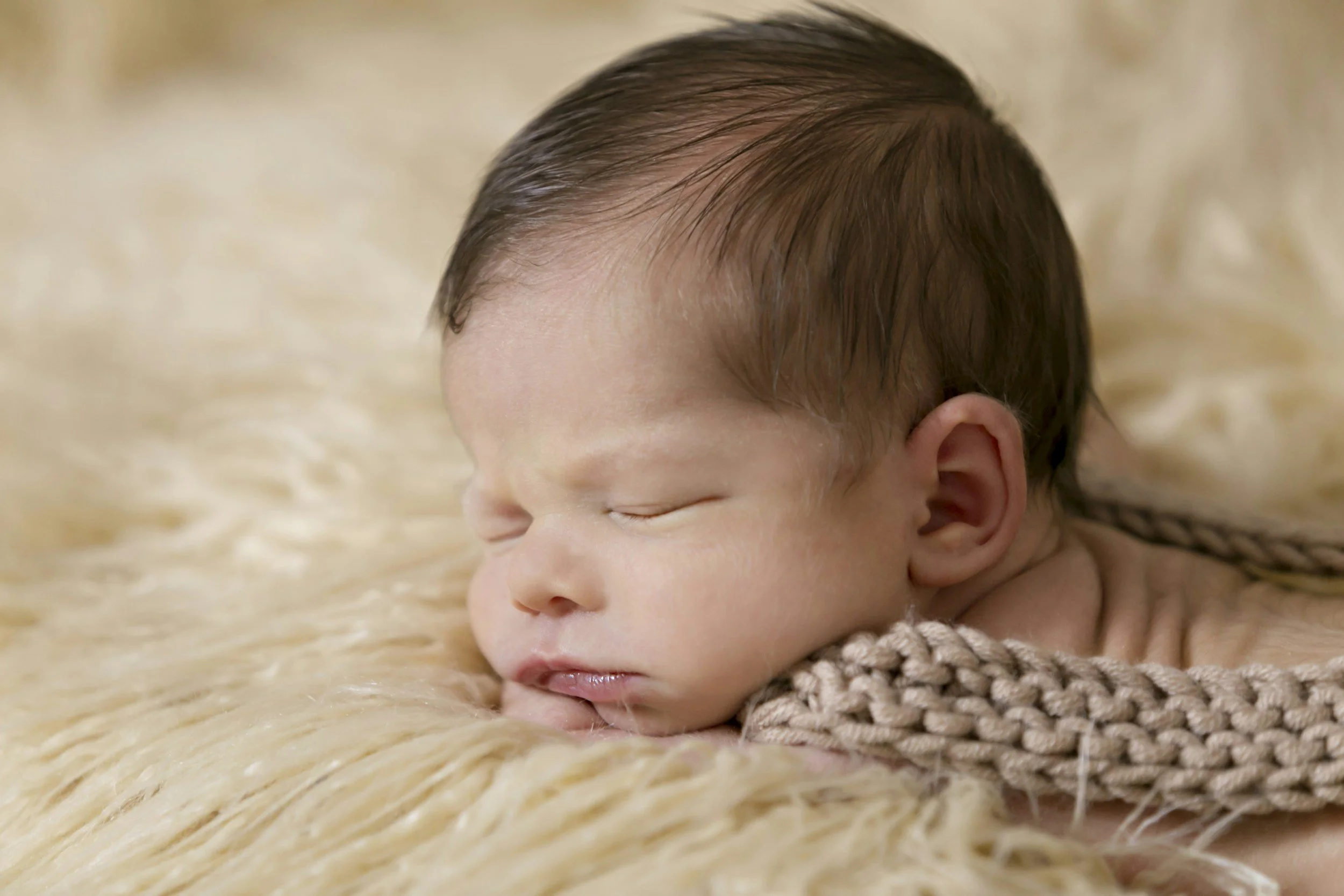 A sleeping baby resting on a soft, fuzzy, cream-colored blanket.