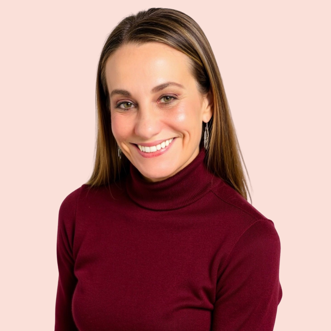 A smiling woman with long brown hair wearing a burgundy turtleneck sweater and earrings against a light pink background.
