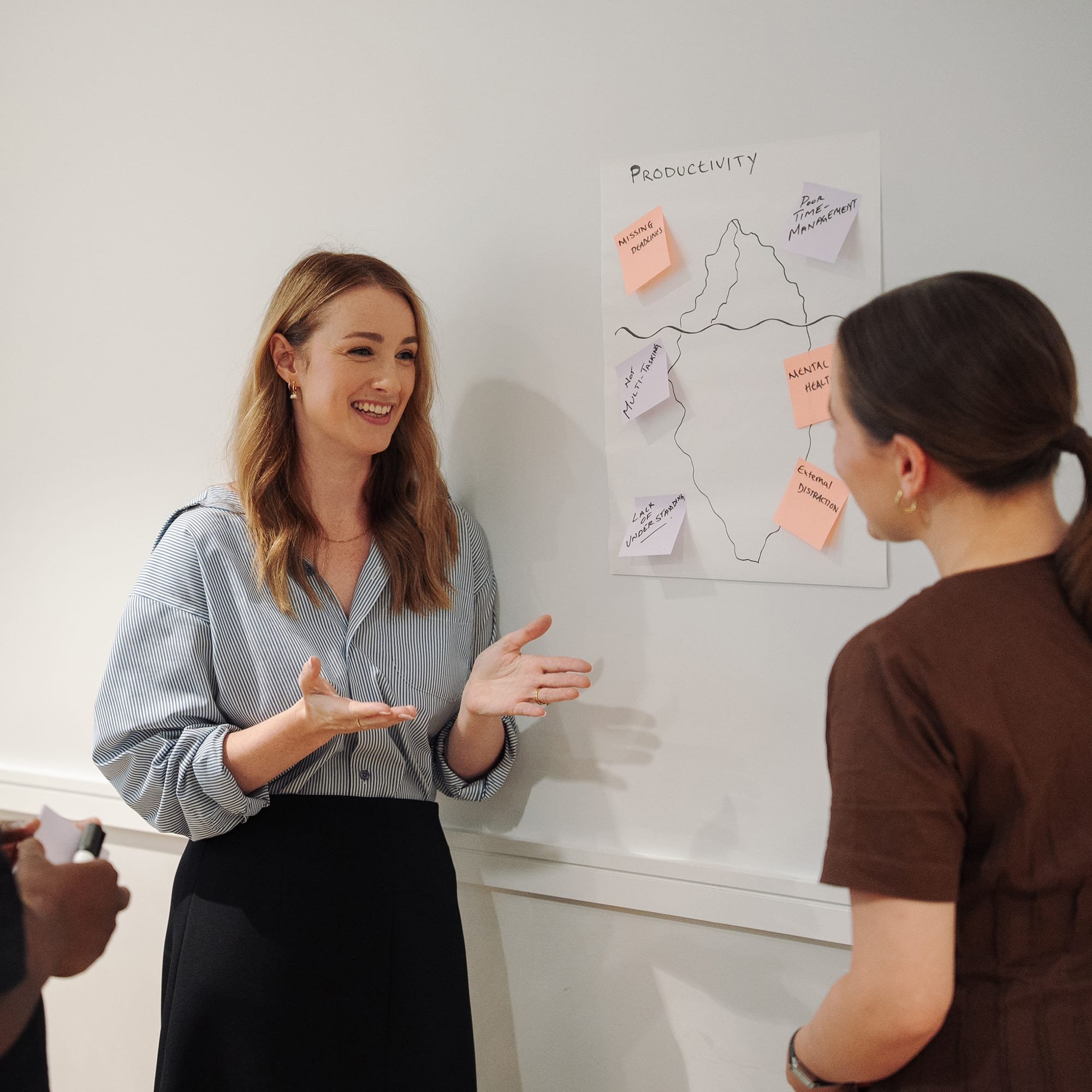 Facilitator leading a workplace communication and productivity workshop, guiding a discussion at a whiteboard with sticky notes and diagrams
